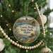 A circular ornament hanging on a Christmas tree, featuring a scenic landscape with mountains, water, and pine trees.