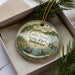 A decorative ornament in a box, featuring a scenic image of Lums Pond State Park, Delaware.