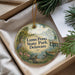A decorative ornament with a scenic image of a pond and surrounding nature, including a bird, is displayed in a box with pine branches.