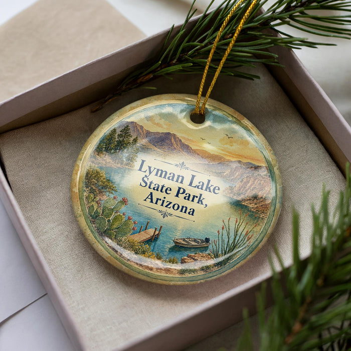 A decorative ornament in a box, featuring a scenic landscape with mountains, water, and a boat, along with the text "Lyman Lake State Park, Arizona".