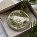 A decorative ornament with a scenic image of a park, featuring a bridge, trees, and water, is displayed in a box.
