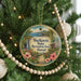 A circular ornament hanging on a Christmas tree, featuring a tropical landscape with a waterfall and hibiscus flowers.