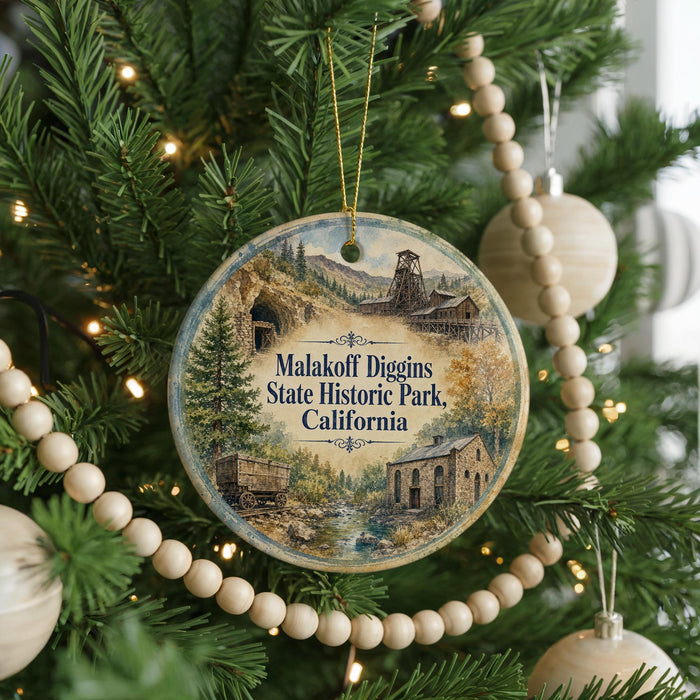 A round ornament hanging on a Christmas tree, featuring a scenic image of Malakoff Diggin's State Historic Park, California.