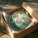 A circular ornament in a box, featuring a painting of a manatee and a bridge, with the text "Manatee Springs State Park, Florida" printed on it.