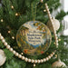 A round ornament hanging on a Christmas tree, featuring a scenic landscape with a path leading to a cliff and trees.