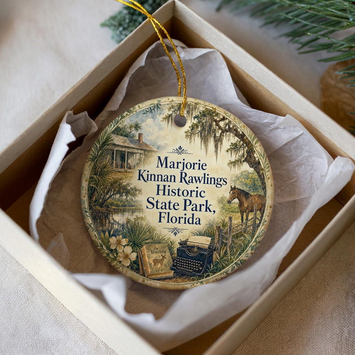 A round ornament with a vintage-style illustration of a house, typewriter, and horse, surrounded by greenery, placed in a white box.