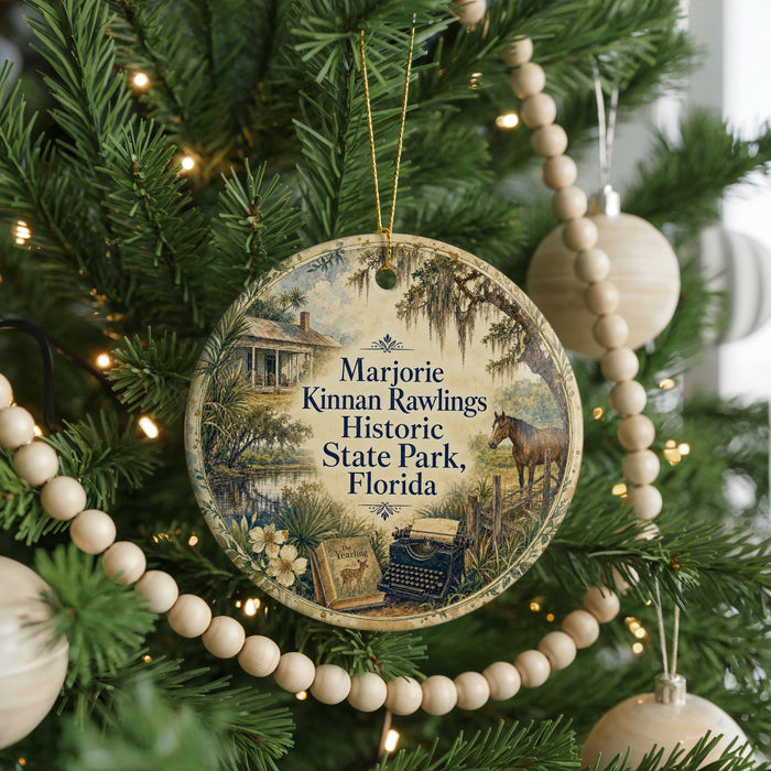 A round ornament hanging on a Christmas tree, featuring a vintage-style illustration of a house and a horse, with the text "Marjorie Kinnan Rawlings Historic State Park, Florida" printed on it.