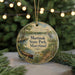 A round ornament with a painting of a lake, boat, and birds, surrounded by greenery and a string of lights.