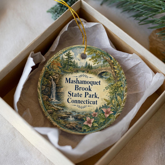 A decorative ornament in a box, featuring a scenic landscape with a waterfall and a bridge.