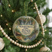 A circular ornament hanging on a Christmas tree, featuring a scenic landscape with a waterfall and a cabin.
