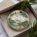A decorative ornament in a box, featuring a scenic image of Meacher State Park in Alabama.