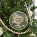 A round ornament hanging on a Christmas tree, featuring a scenic image of a park with a lake and a bridge.