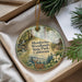 A round ornament with a deer and forest scene, hanging from a string, placed inside a box with pine branches.