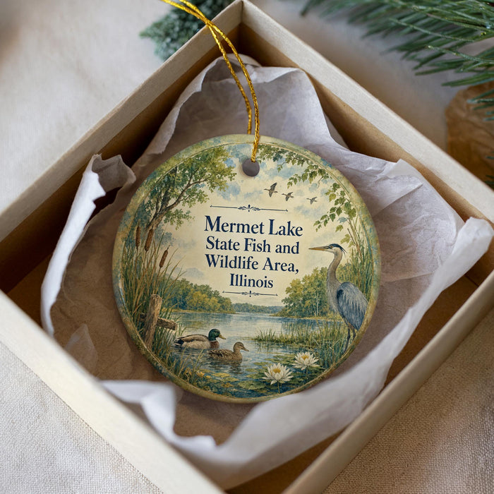 A round ornament with a painting of ducks and a bird in a natural setting, placed in a box with a white tissue paper lining.