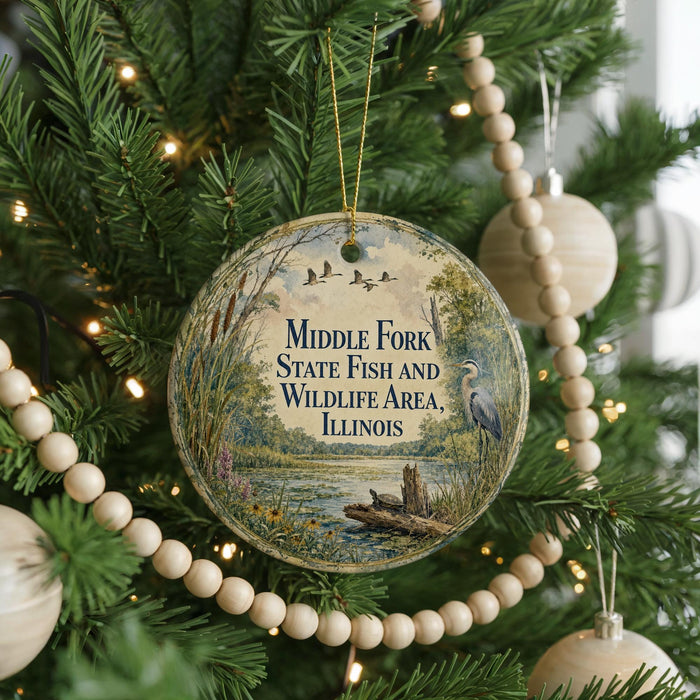 A round ornament hanging on a Christmas tree, featuring a scenic image of a lake surrounded by trees and wildlife.