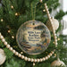 A round ornament hanging on a Christmas tree, featuring a scenic landscape with a lake, trees, and a cabin.