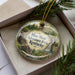 A decorative ornament with a scenic image of a forest and a waterfall, along with the text " Mine Made Adventure Park, Kentucky" on it, is displayed in a box.