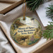A decorative ornament with a scenic landscape featuring a bird, a castle, and a path, placed in a box with pine branches.
