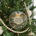 A round ornament hanging on a Christmas tree, featuring a scenic landscape with a bridge and trees.