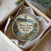 A decorative ornament in a box, featuring a moose and a scenic landscape with a lake and pine trees.