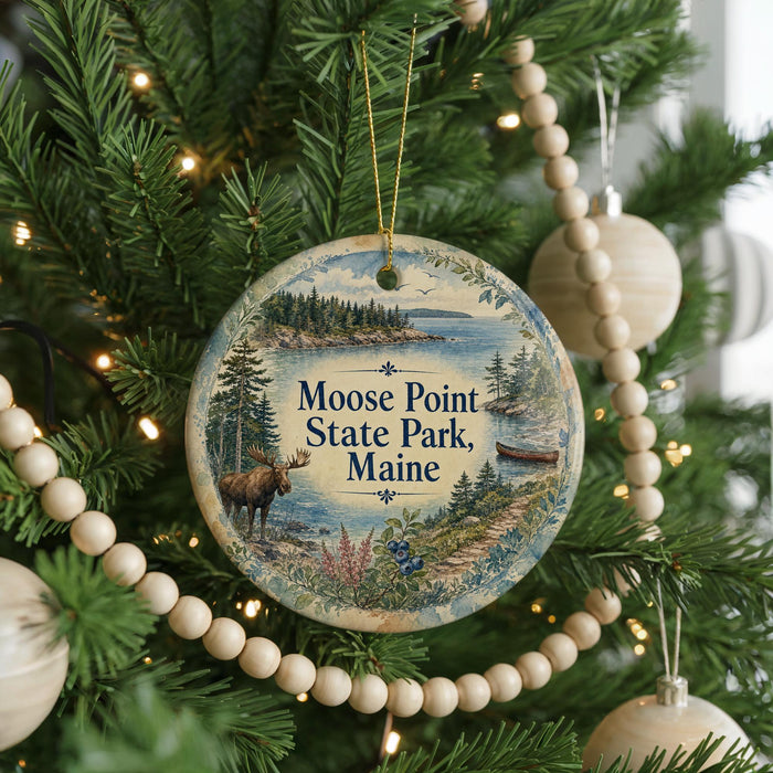 A circular ornament hanging on a Christmas tree, featuring a moose and a scenic landscape of Moose Point State Park, Maine.