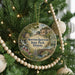 A round ornament hanging on a Christmas tree, featuring a scenic landscape with a bridge and a waterfall.
