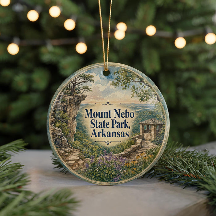 A round ornament with a painting of a scenic landscape, featuring a mountain, trees, and a building, hanging from a string.