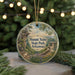 A round ornament with a painting of a scenic landscape, featuring a mountain, trees, and a building, hanging from a string.
