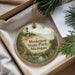 A round ornament with a lighthouse and a scenic landscape, placed in a box with pine branches.