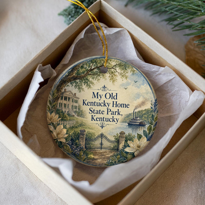 A decorative ornament in a box, featuring a scenic image of a house, trees, and a river, with the text "My Old Kentucky Home State Park Kentucky" printed on it.