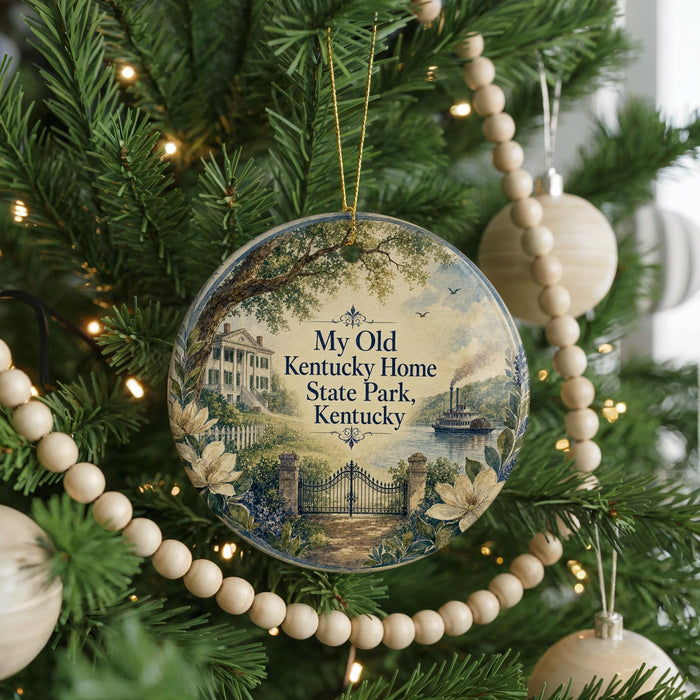 A round ornament hanging on a Christmas tree, featuring a scenic image of Kentucky State Park with a house, trees, and a river.