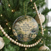 A round ornament hanging on a Christmas tree, featuring a scenic image of Kentucky State Park with a house, trees, and a river.