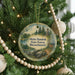 A round ornament hanging on a Christmas tree, featuring a scenic landscape with a forest, a lake, and a deer.