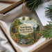 A decorative ornament with a scenic forest landscape, featuring a waterfall and pine trees, is displayed in a box with pine branches.