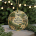 A round ornament with a painting of a park scene, featuring a house, trees, and a bridge, hanging from a string.