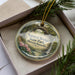 A decorative ornament in a box, featuring a scenic landscape with a natural bridge and greenery.