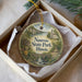 A decorative ornament in a box, featuring a scenic landscape with a river, bridge, and buildings, along with the text "Nauvoo State Park, Illinois".
