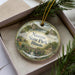 A decorative ornament in a box, featuring a scenic landscape with a bridge and buildings, along with the text "Nauwooo State Park, Illinois".