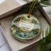 A decorative ornament with a scenic image of the Navarro River and Redwoods State Park in California, displayed in a box with pine branches.