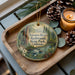 A decorative ornament featuring a scenic image of the Navarro River and Redwoods State Park in California, with pine cones and a lit candle on a wooden tray.