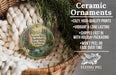 Ceramic ornaments, featuring a round ornament with a forest scene and text, hanging in a basket with pine branches.