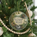 A Christmas tree decorated with ornaments, including a round ornament with a scenic image of a forest and a stream, and beaded ornaments.