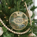 A round ornament hanging on a Christmas tree, featuring a scenic landscape with a lake, bridge, and trees.