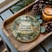 A wooden tray with a decorative ornament featuring a scenic landscape of Nickerson State Park, Massachusetts, and pine cones.