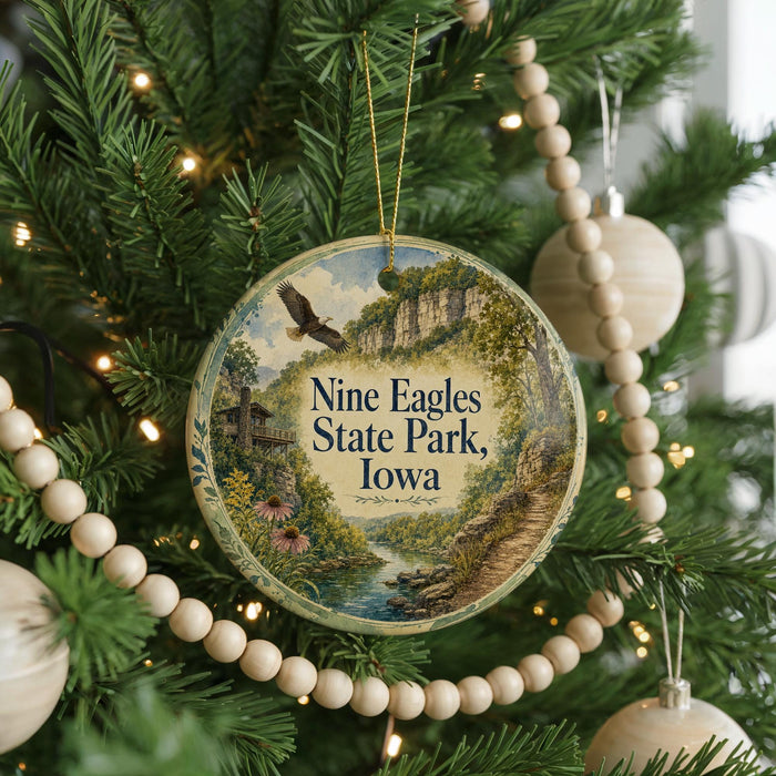 A round ornament hanging on a Christmas tree, featuring a scenic landscape with a river, cliffs, and a bird in flight.