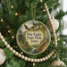 A round ornament hanging on a Christmas tree, featuring a scenic landscape with a river, cliffs, and a bird in flight.