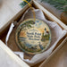 A round ornament with a lighthouse and a seagull, surrounded by a scenic landscape, is displayed in a box.