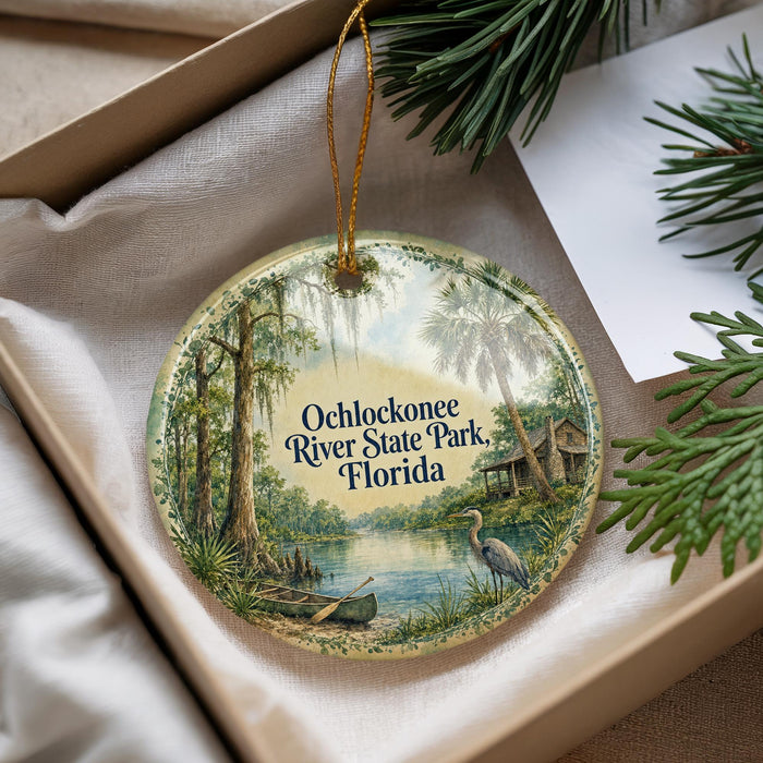 A decorative ornament with a painting of a river and a bird, placed in a box with pine branches.