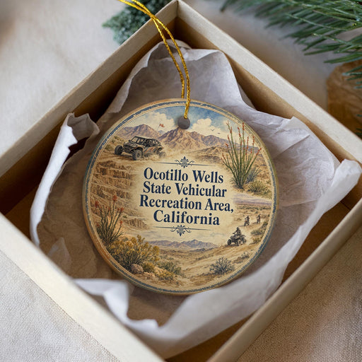A round ornament with a desert landscape and a vehicle, placed in a box with a white tissue paper lining.