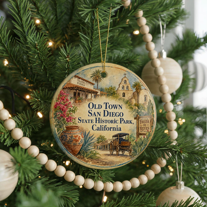 A round ornament hanging on a Christmas tree, featuring an illustration of a historic building and a wagon, with the text "Old Town San Diego State Historic Park, California" and "Fiesta Reves" displayed.